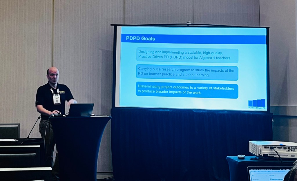 Sam Otten in a conference room standing next to a slide that states the PD goals of the PDPD project.